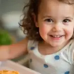 A smiling toddler enjoying a meal with homemade baby food puree.