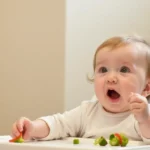 A baby sitting in a high chair, reacting to food with an expression of surprise while holding small vegetable pieces, illustrating picky eating habits.
