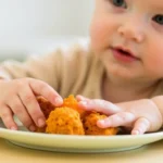 A baby exploring a nutritious baby-led weaning meal with mashed sweet potato on a slice of baked potato.