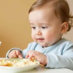 A baby enjoying a plate of nutritious homemade infant food paired with a cup of milk on a highchair.
