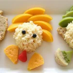 Fun and nutritious homemade baby food arranged as cute animal shapes using rice, whole wheat bread, fruit slices, and berries.